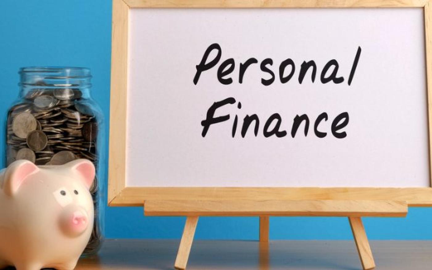 An easel with a picture that says "Personal Finance". Next to the easel is a piggy bank and a jar of coins.