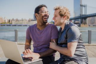A gay couple looking at a computer together. They are both smiling